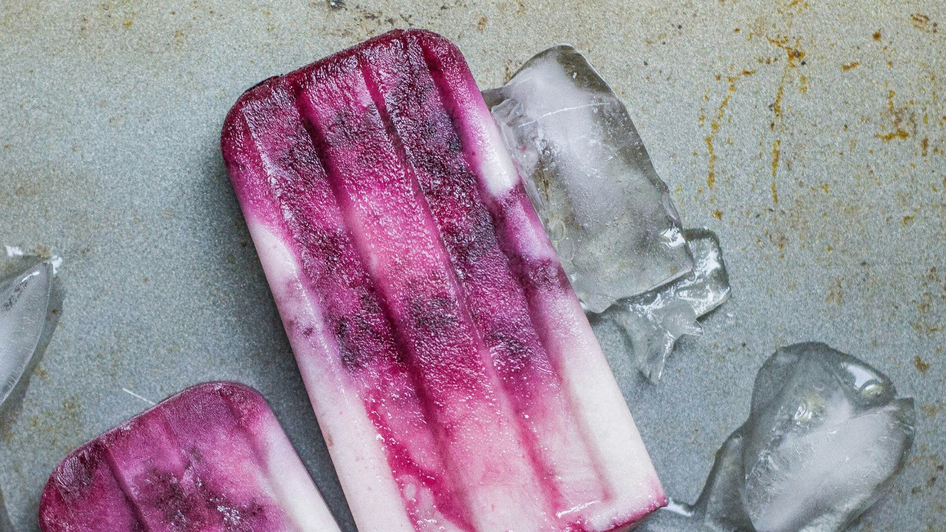 purple and white ice pop lying on wet ground with ice