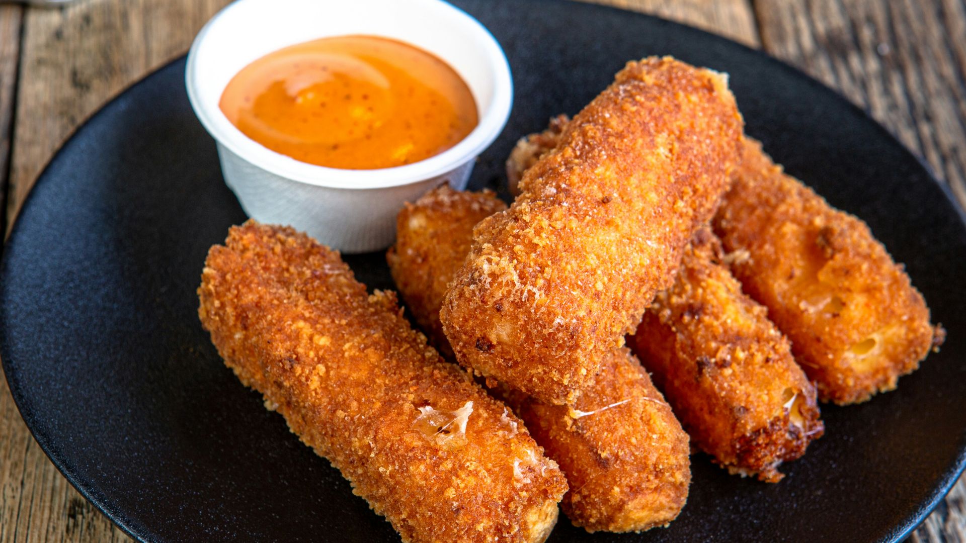 A black plate topped with fried food next to a cup of dipping sauce