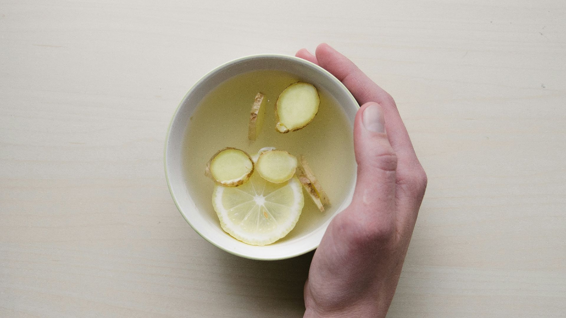 person holding white bowl with sliced lime and ginger inside