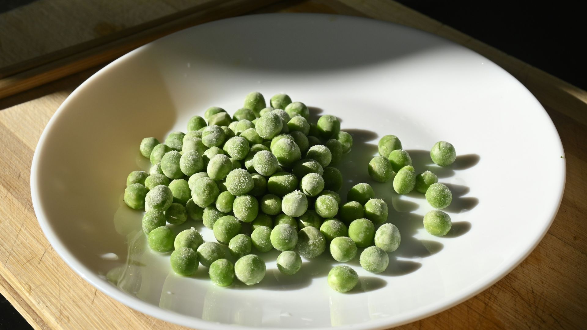 a white plate topped with green peas next to chopsticks