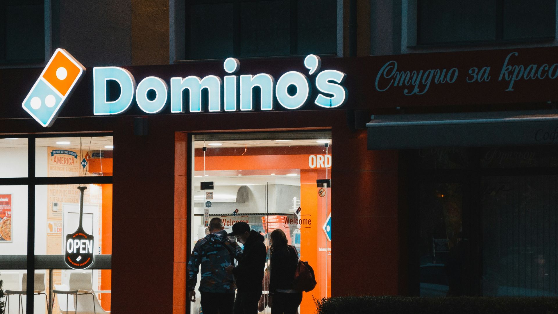 a group of people standing outside of a domino's store