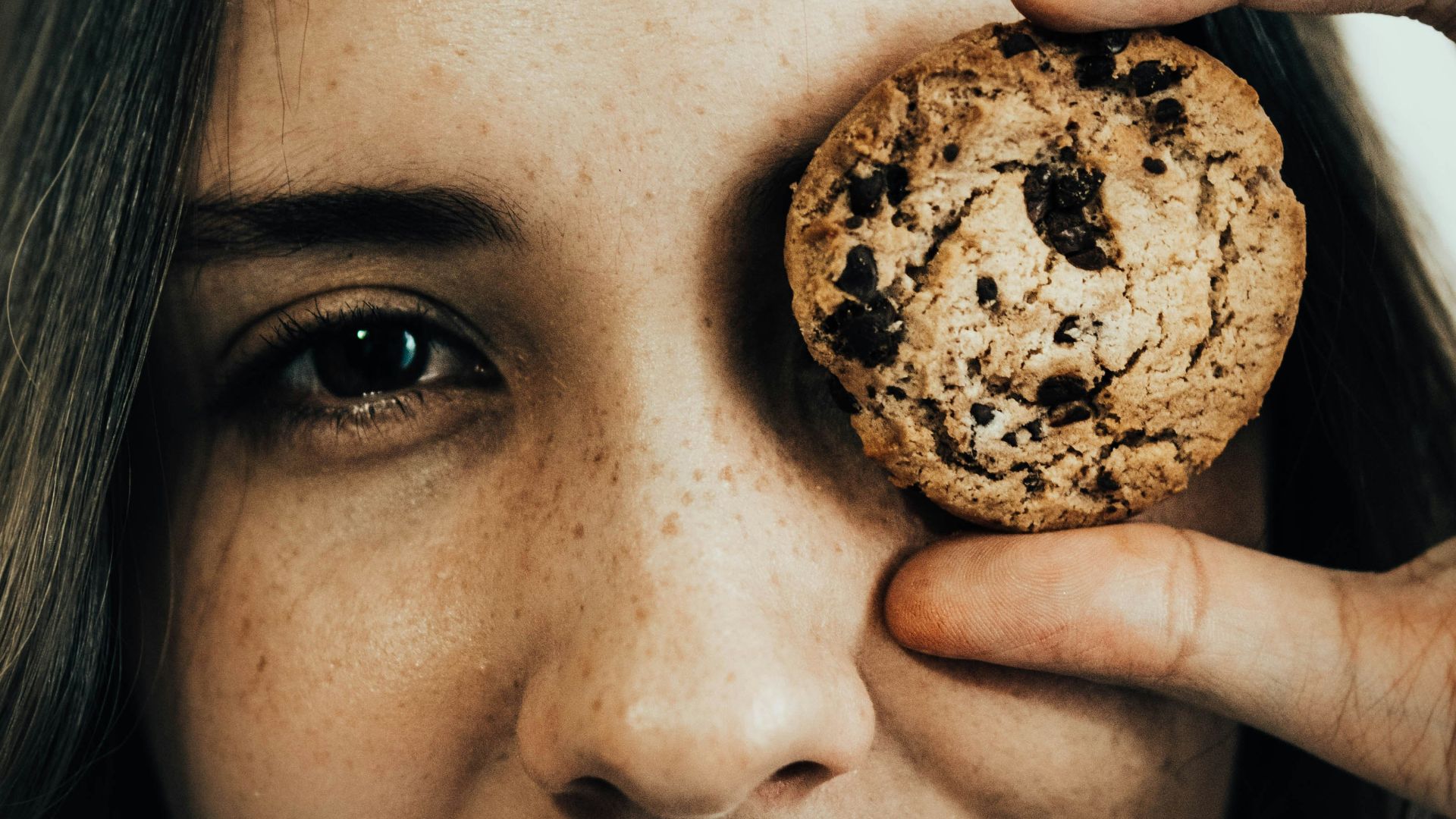 a woman holding a chocolate chip cookie up to her eye
