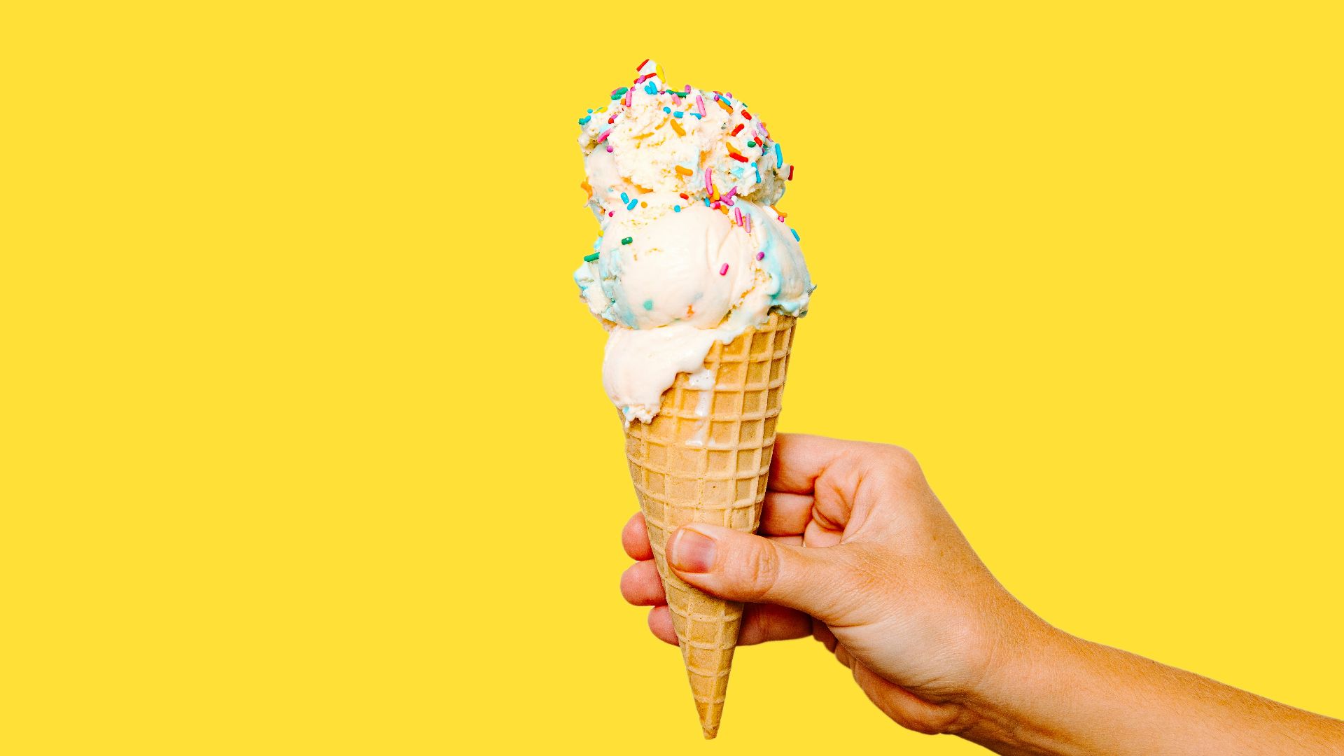 A hand holding an ice cream cone with sprinkles