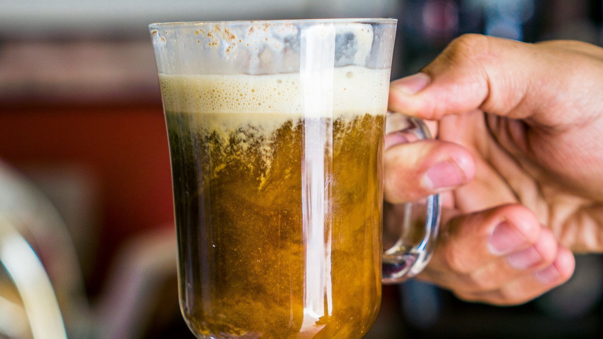 person holding glass mug with brown liquid