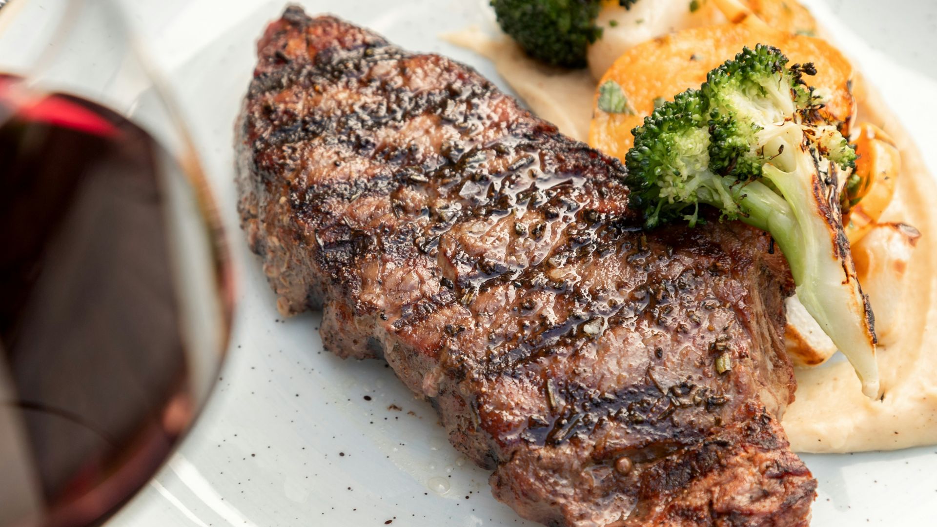 a white plate topped with meat and veggies next to a glass of wine