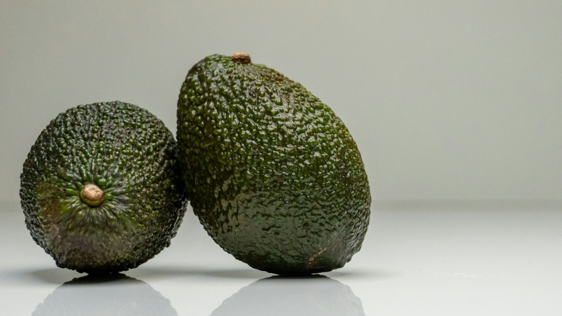 two avocados sitting side by side on a white surface