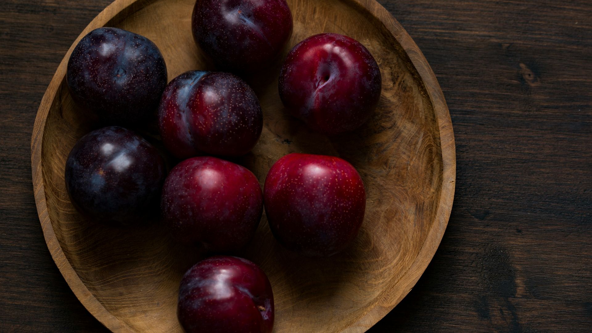 red plum fruits on round brown wooden plate