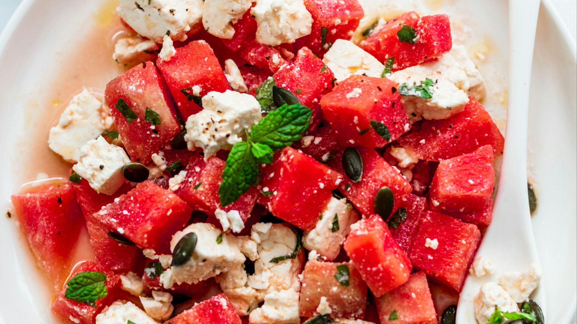 a plate of watermelon and feta salad next to a glass of water
