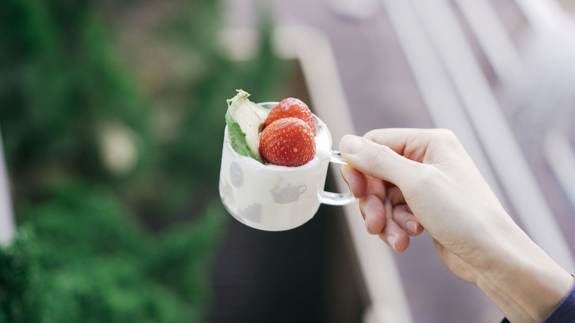 person holding white ceramic mug with strawberry and cream