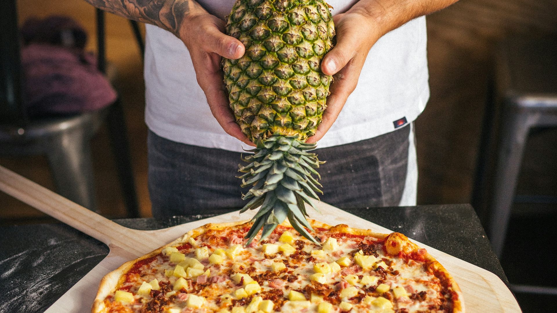 a man holding a pineapple on top of a pizza