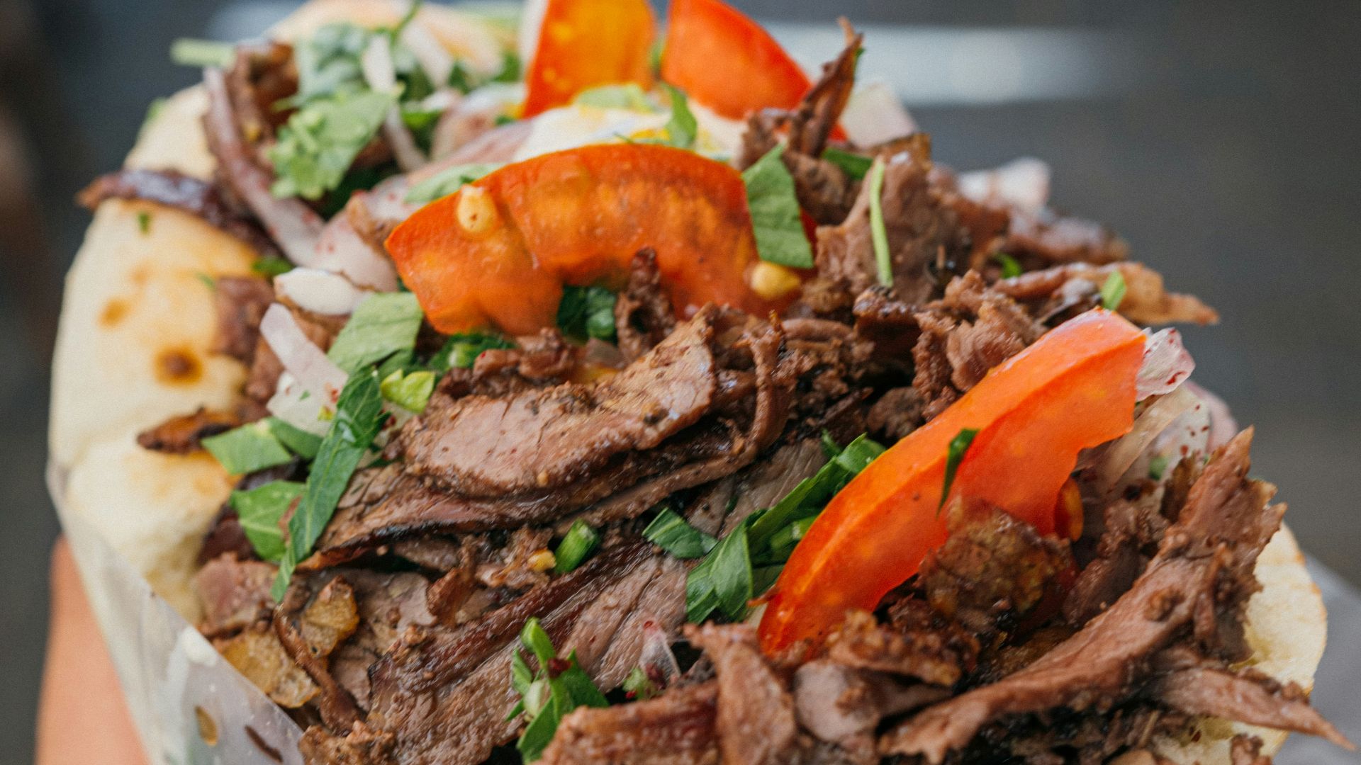 a person holding a sandwich with meat and vegetables