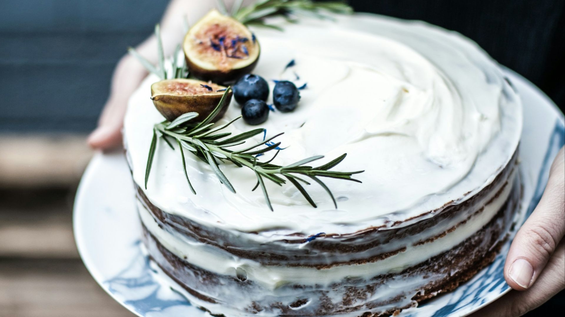 person holding round white icing-covered cake with blue berry on top
