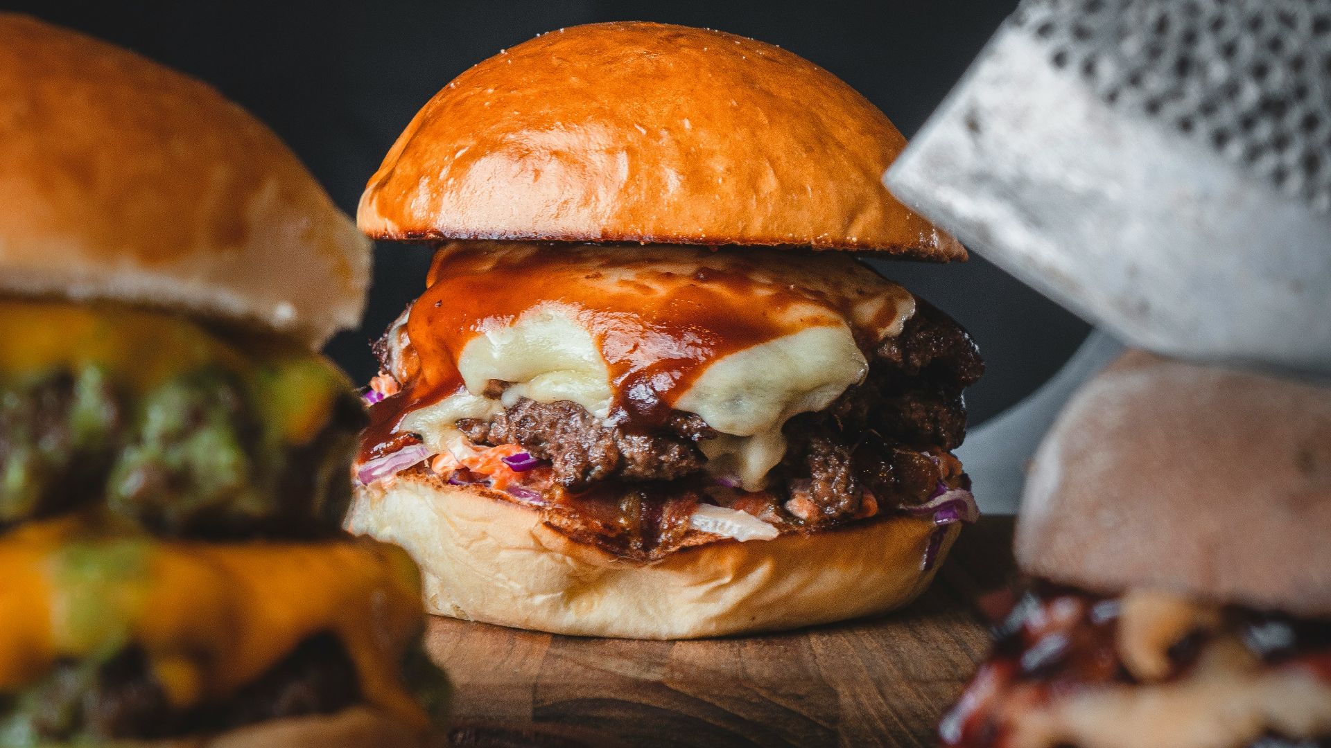 three hamburgers on a cutting board with a cheese grater