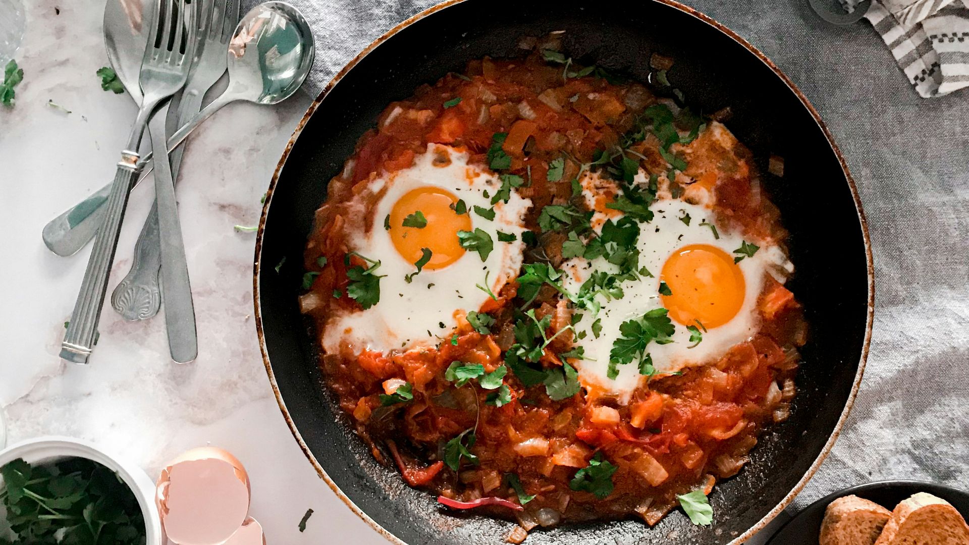 tomato soup on black cooking pan beside stainless steel fork and bread knife