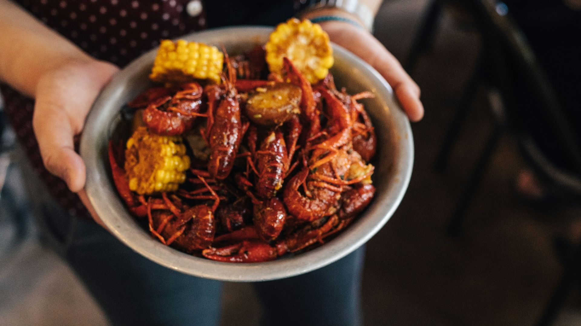 person holding bowl of shrimp with slice of corn dish