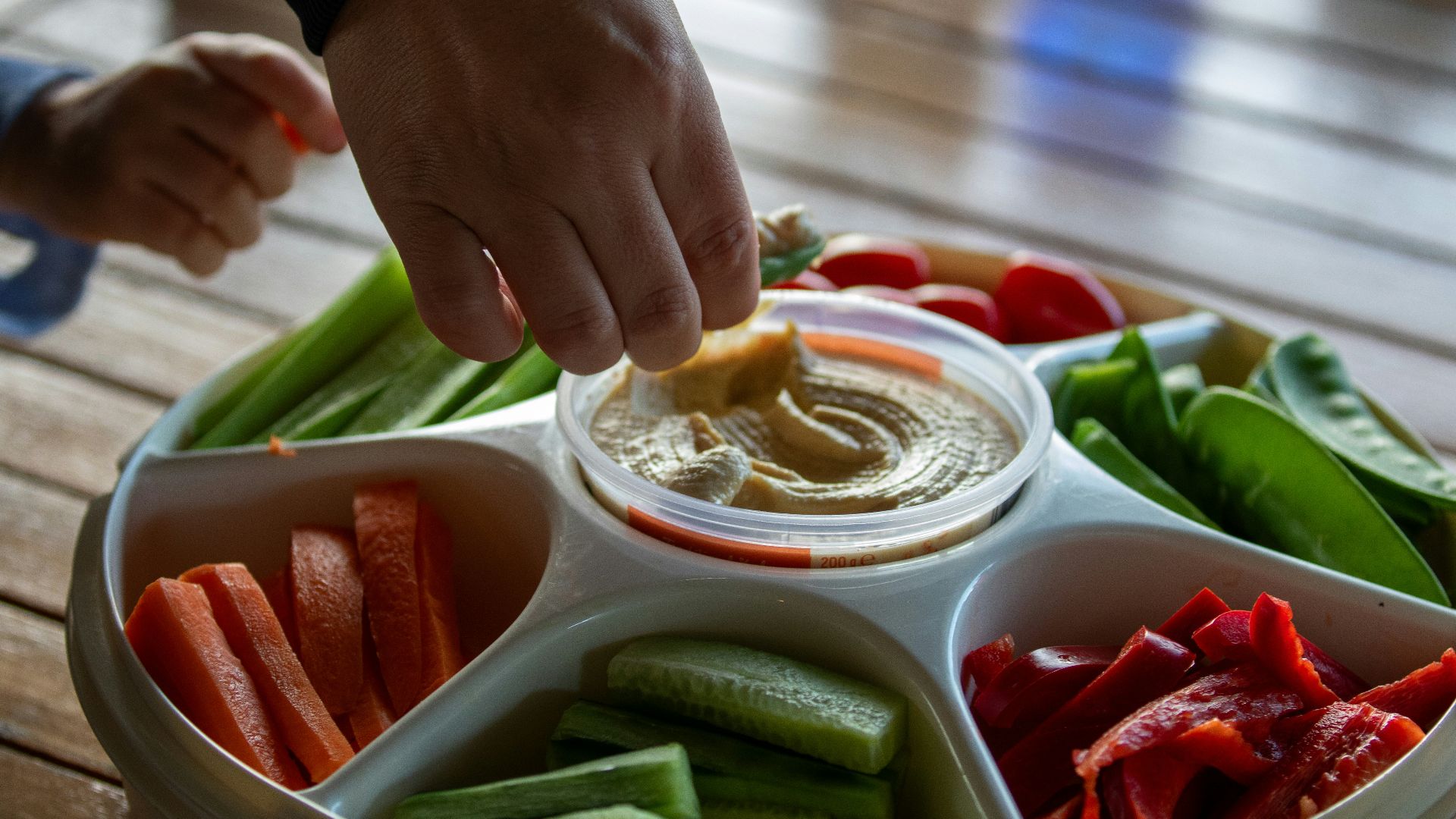 A person dipping dip into a bowl of vegetables