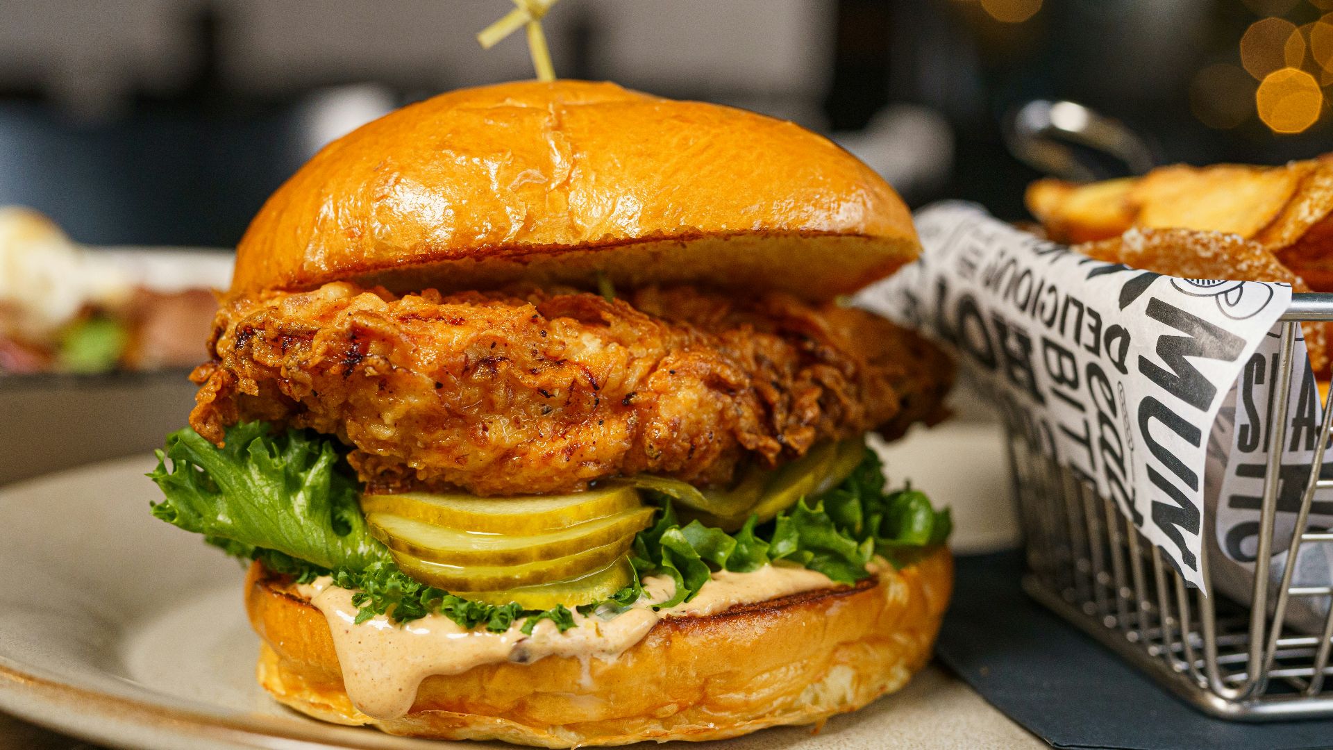a chicken sandwich on a plate next to a basket of fries