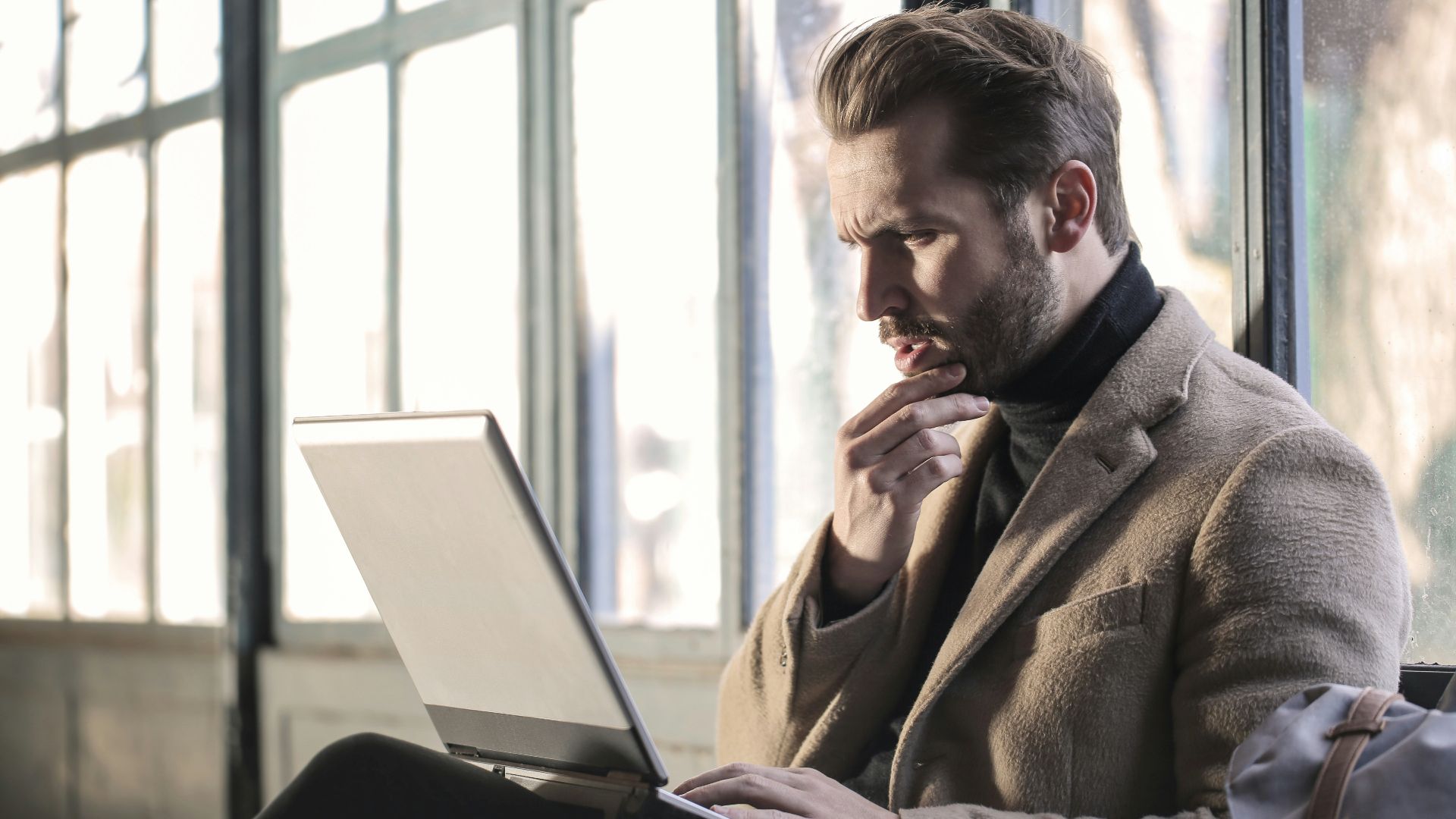 man holding his chin facing laptop computer