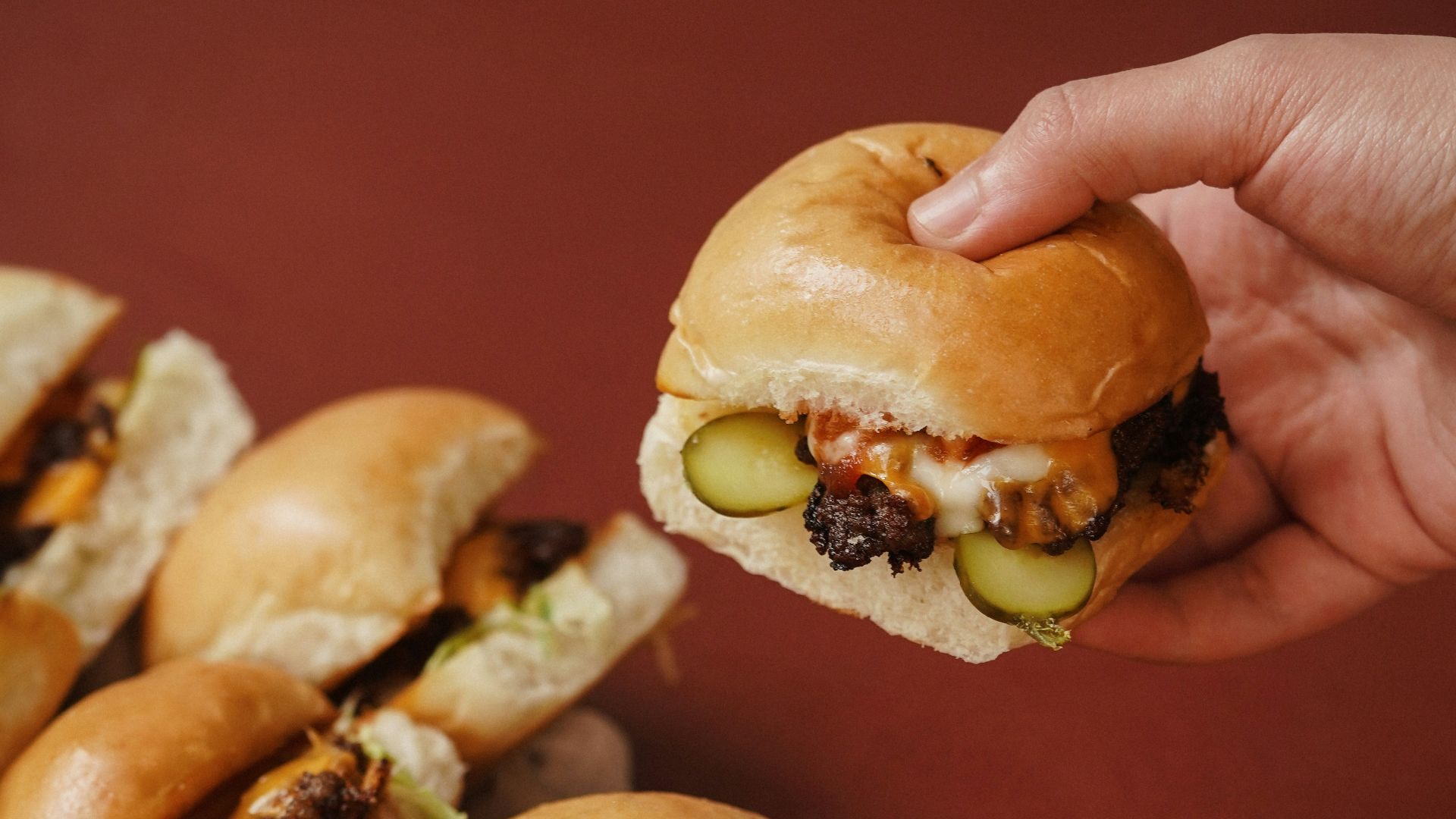a hand holding a sandwich over a pile of mini sandwiches