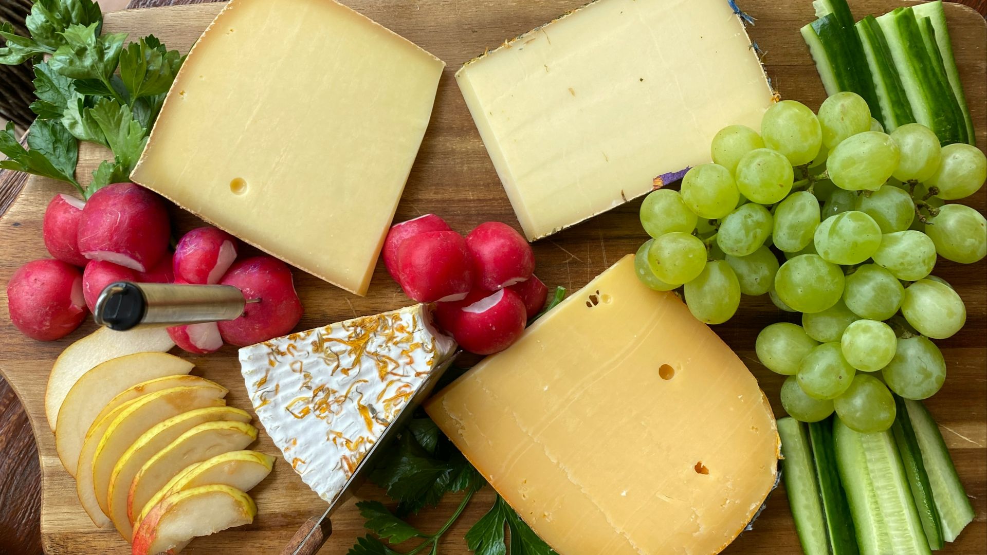 a wooden cutting board topped with cheese and fruit
