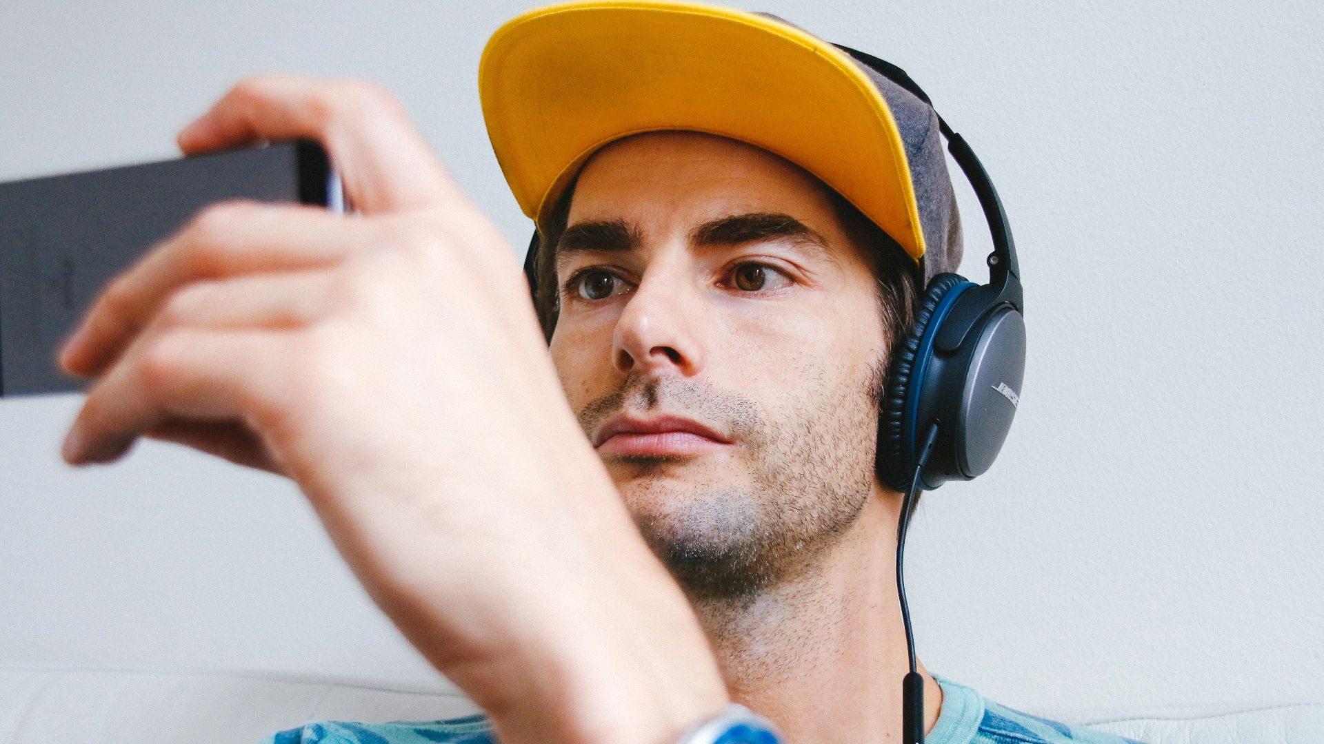 man wearing black corded headphones while holding phone