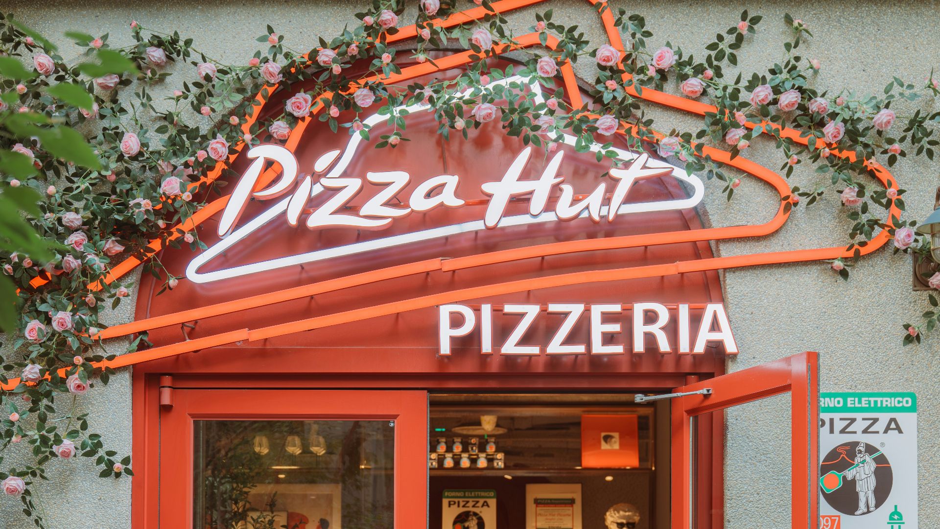 Pizza hut pizzeria entrance with neon sign and flowers