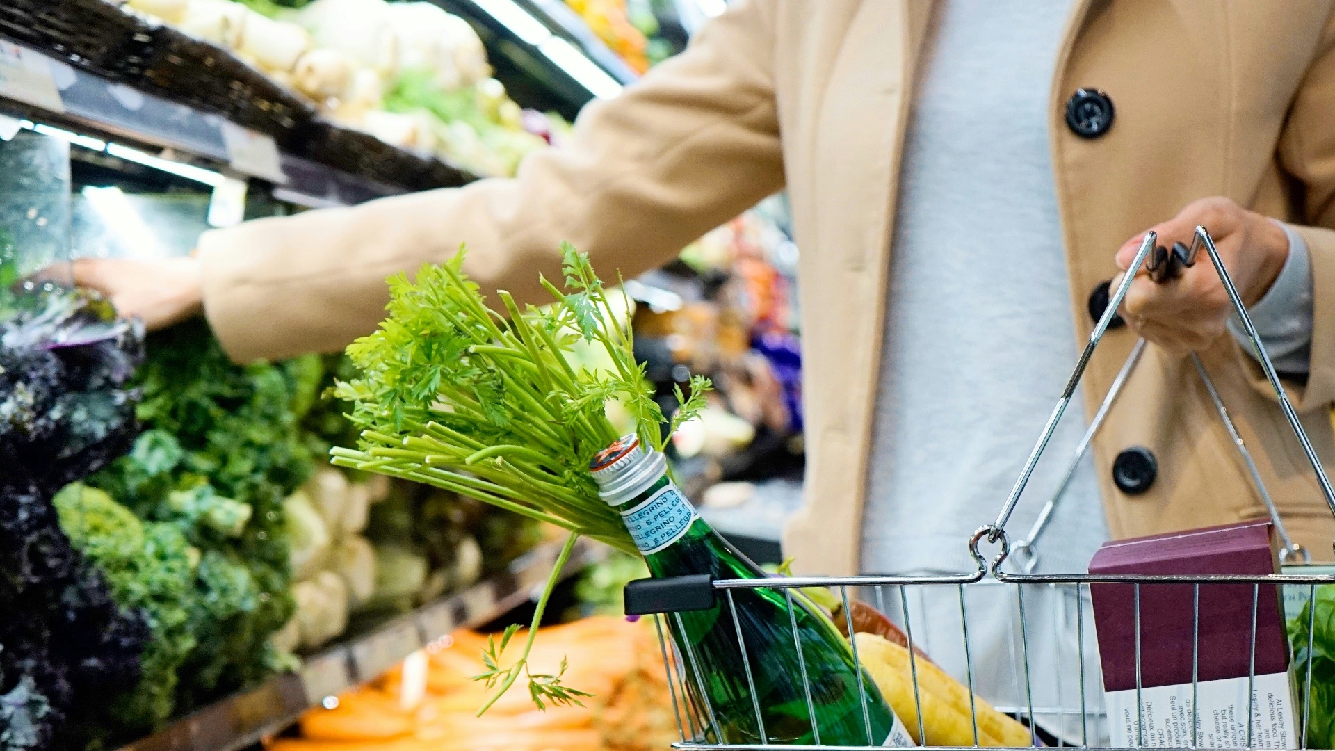 woman in white coat holding green shopping cart