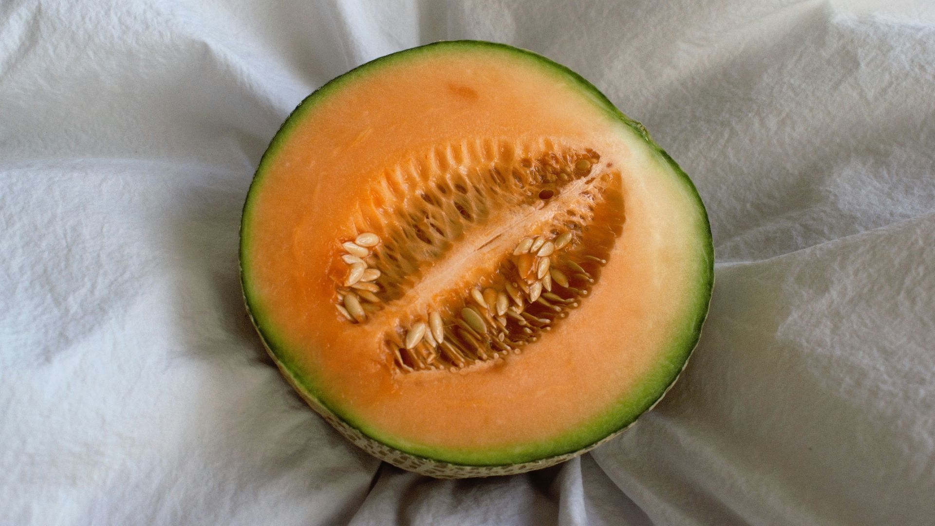 a cut in half melon sitting on top of a white cloth