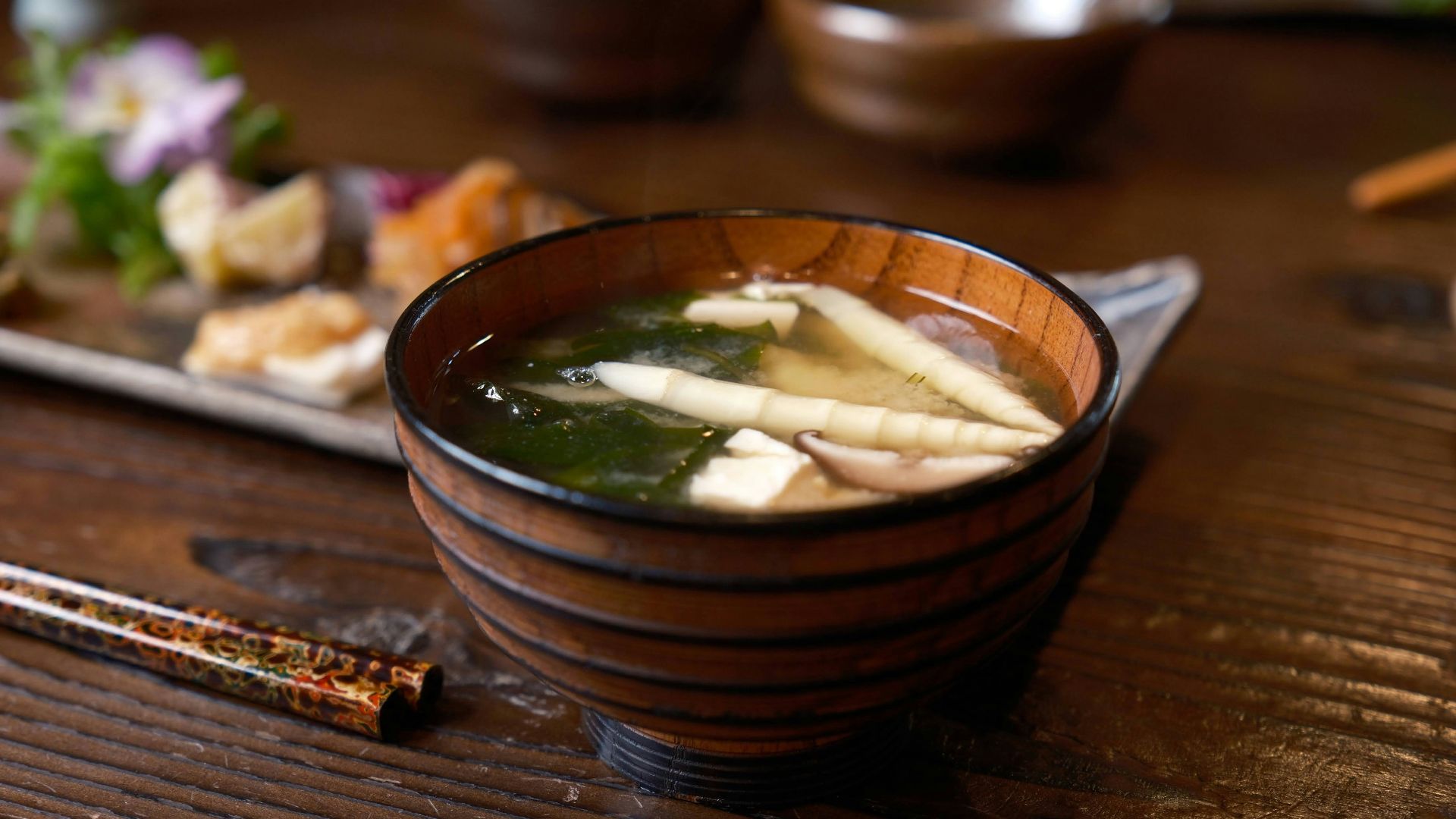 a wooden bowl filled with soup next to chopsticks