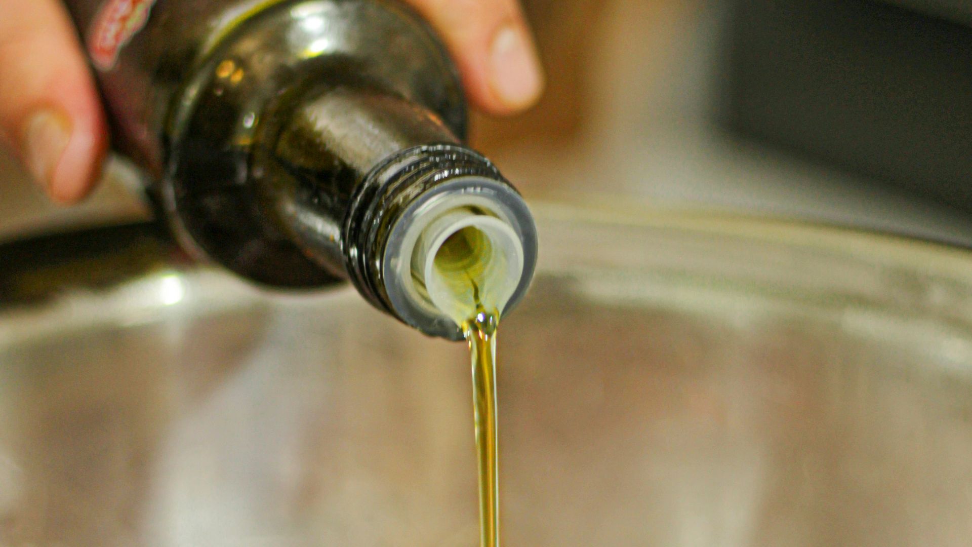 a person pouring olive into a pot filled with meat
