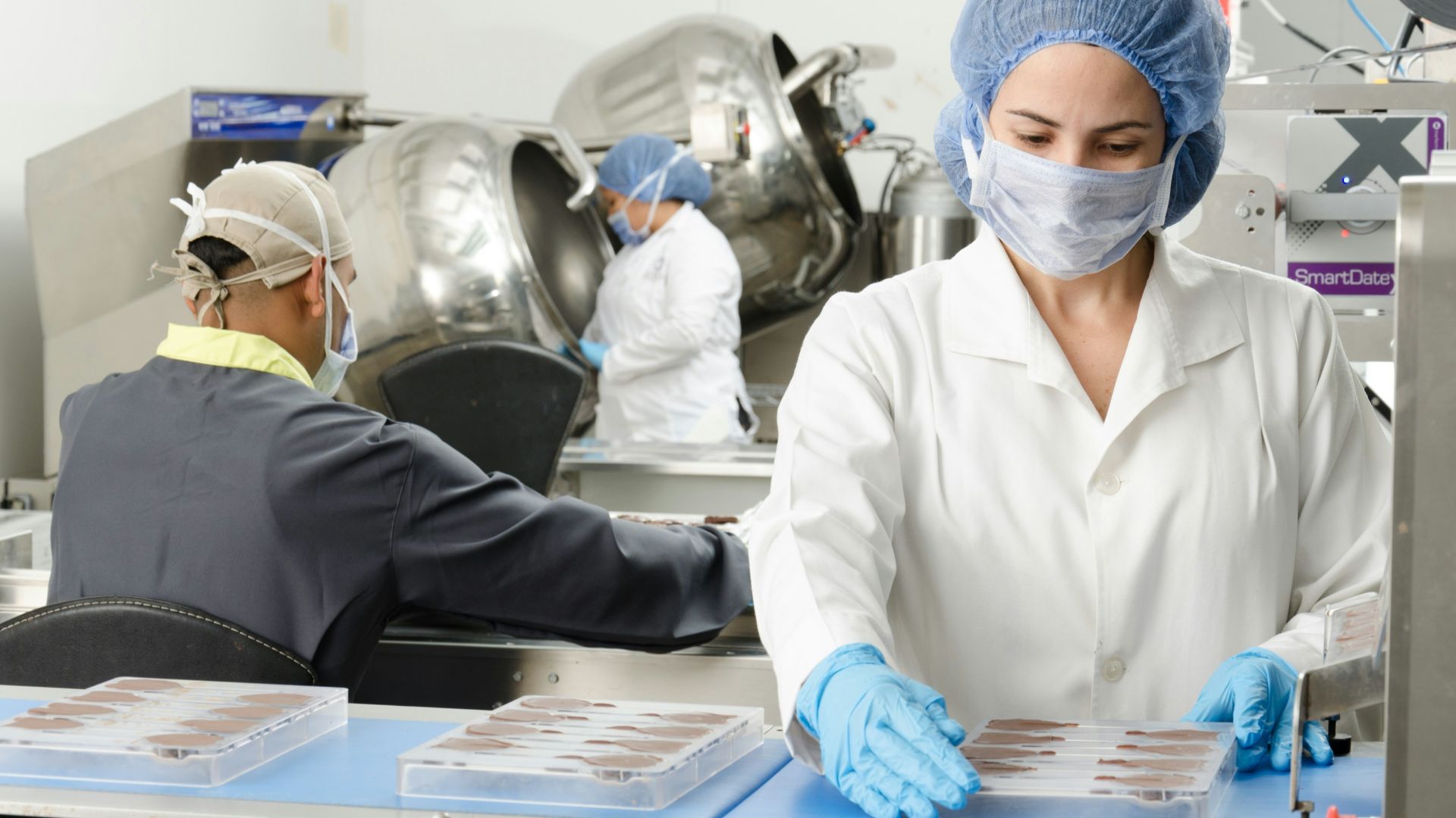 three people inside factory wearing masks and coats