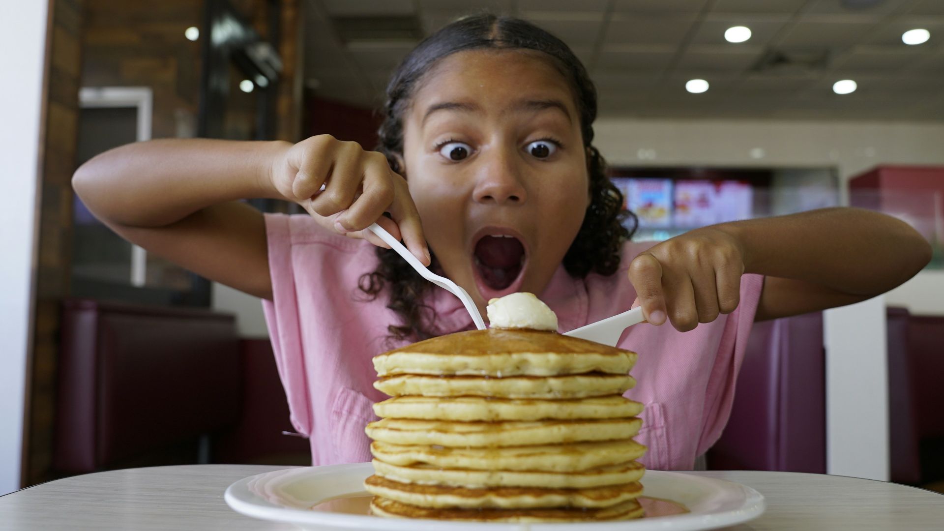 Girl with surprised expression eating stack of pancakes