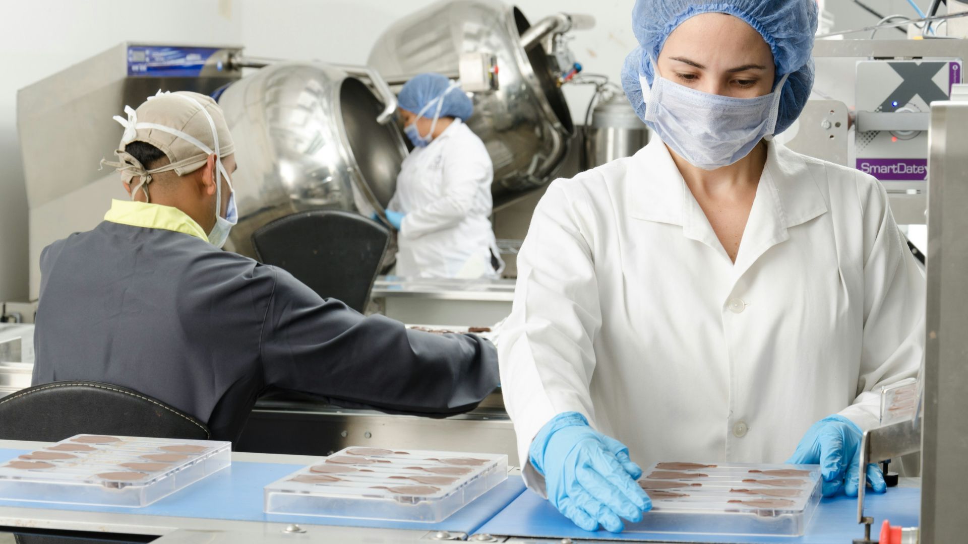 three people inside factory wearing masks and coats