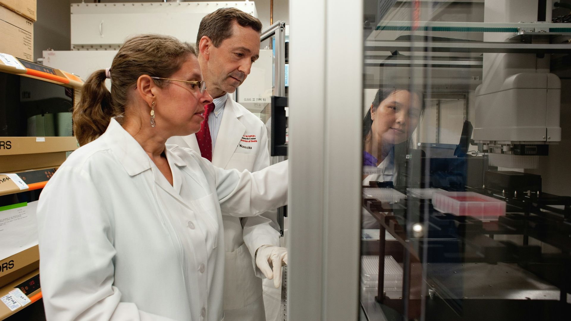 a man and a woman in lab coats looking at something in a cabinet