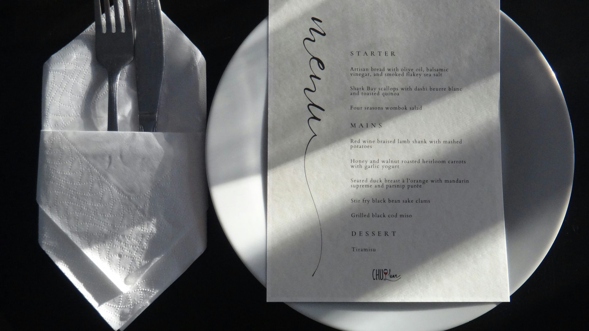 A white plate topped with a piece of paper next to a fork and knife