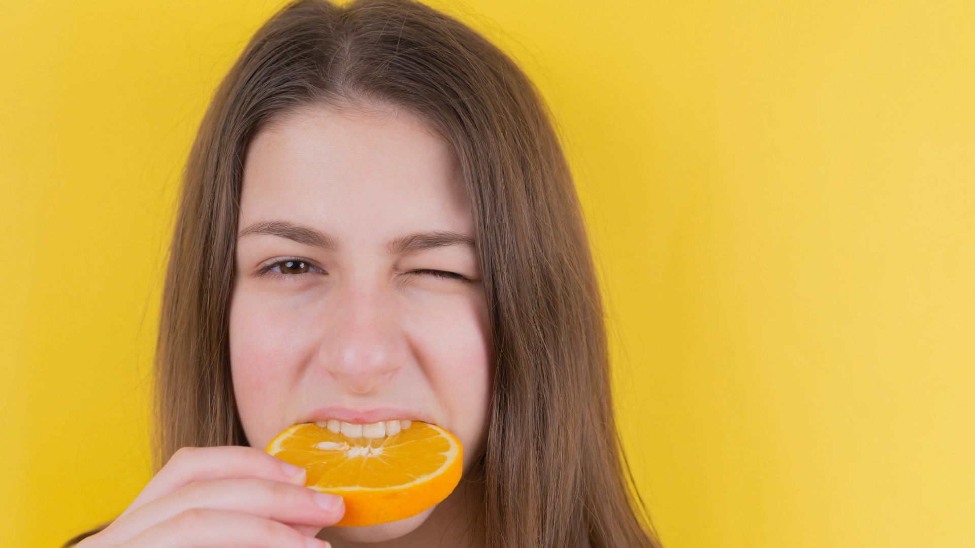 girl holding orange fruit in front of yellow wall