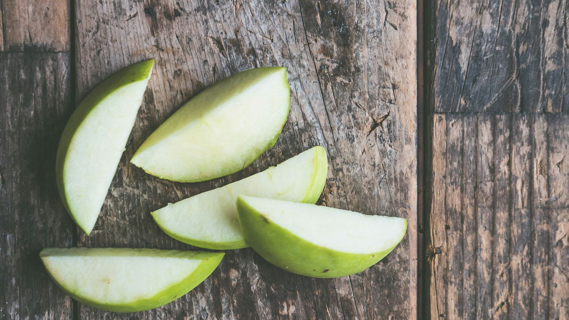 five green apple slices on brown wooden panel