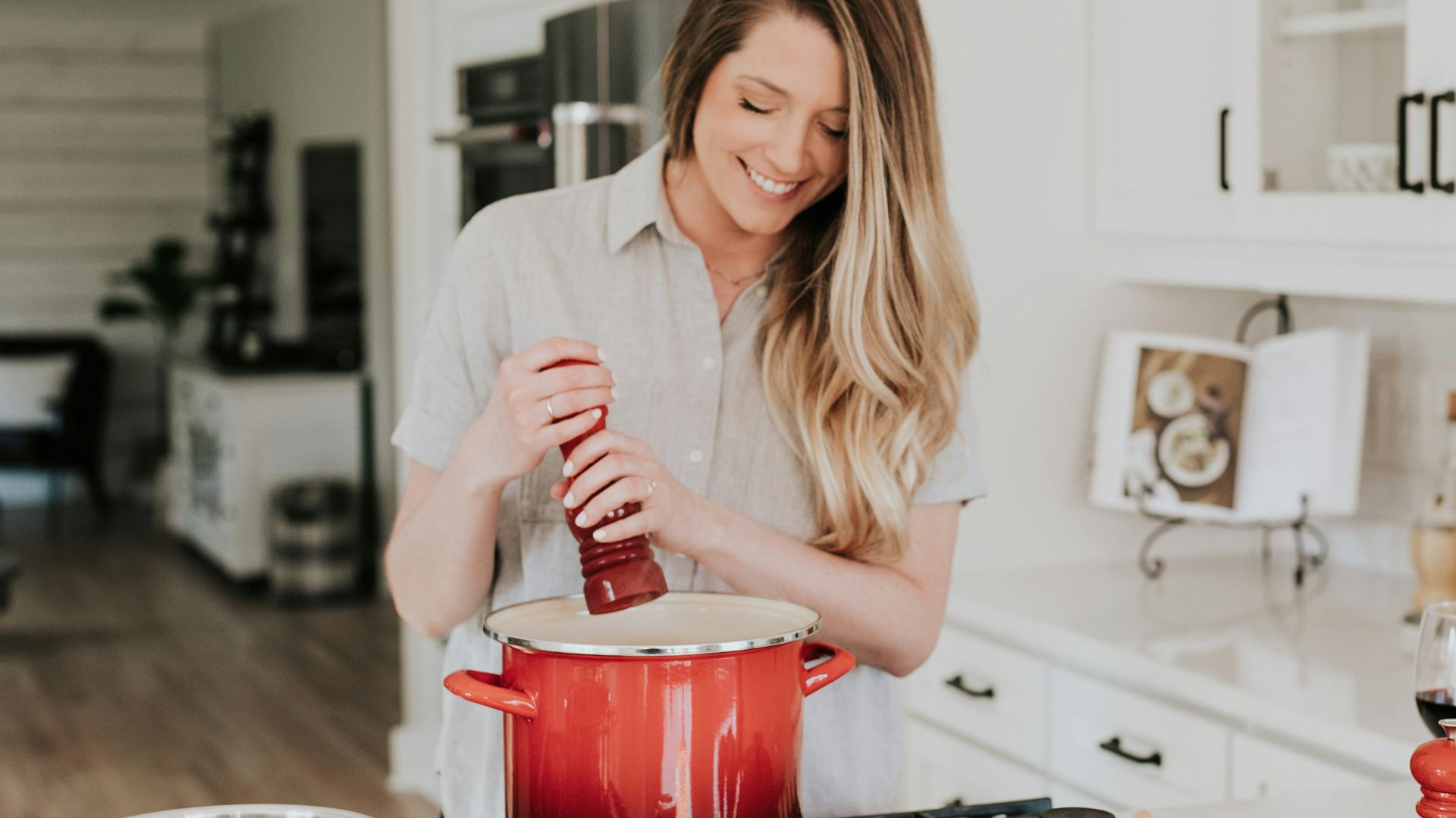 smiling woman standing and putting pepper on stock pot