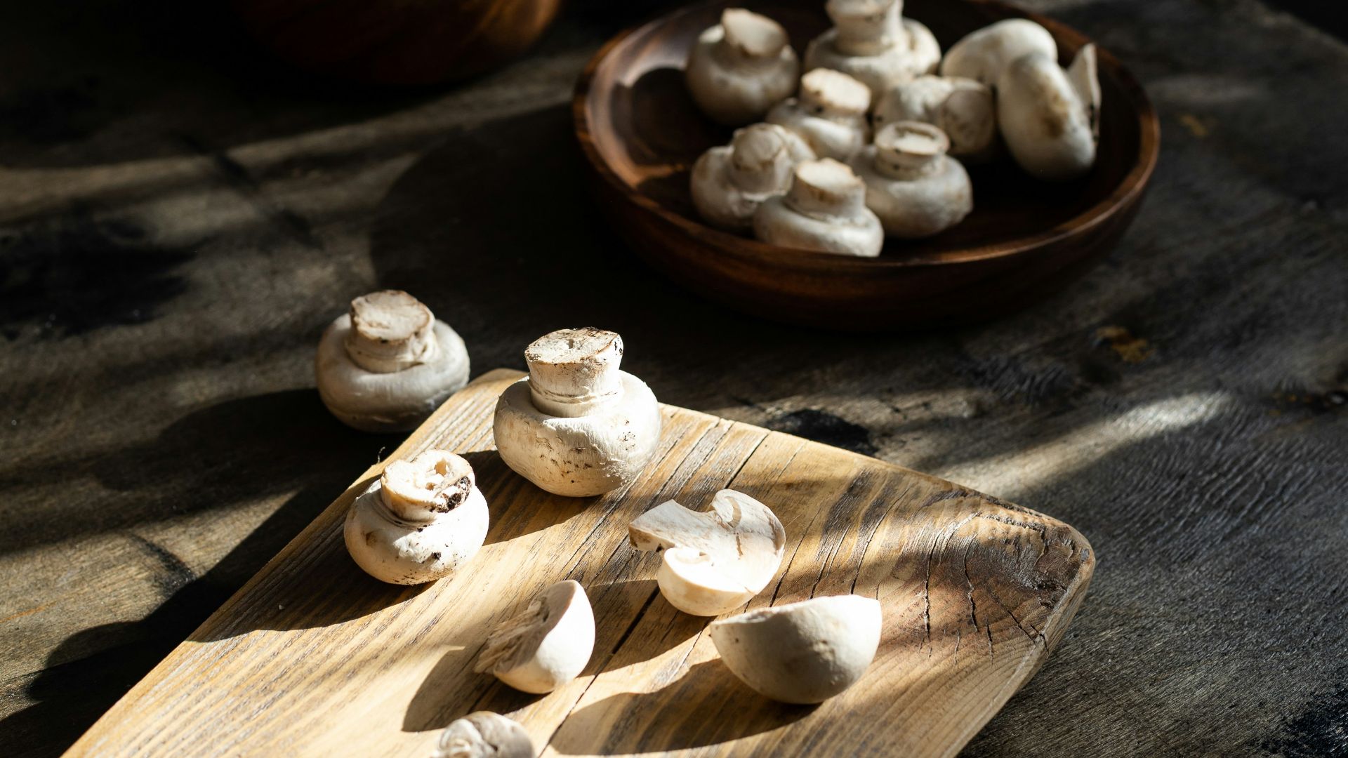 a wooden cutting board topped with mushrooms next to a bowl of mushrooms
