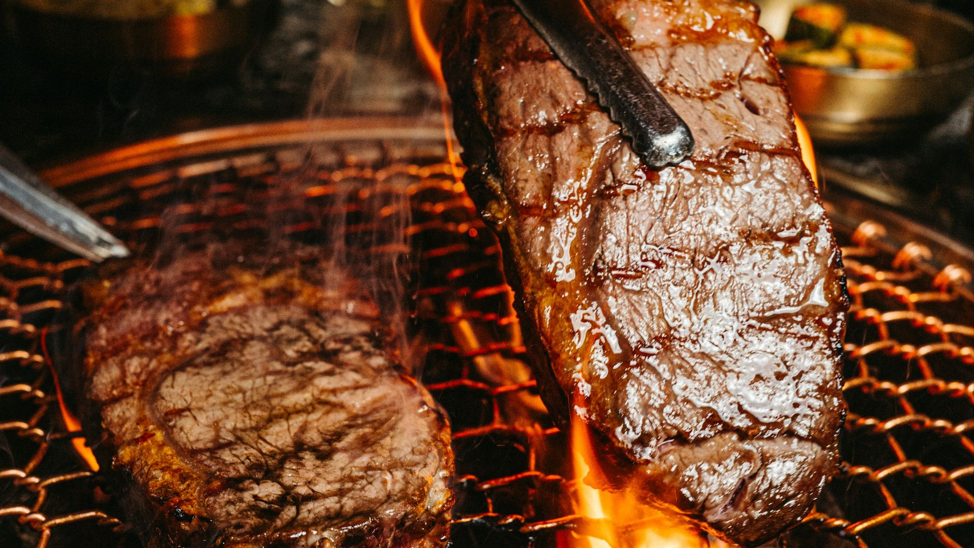 a steak being cooked on a grill with tongs