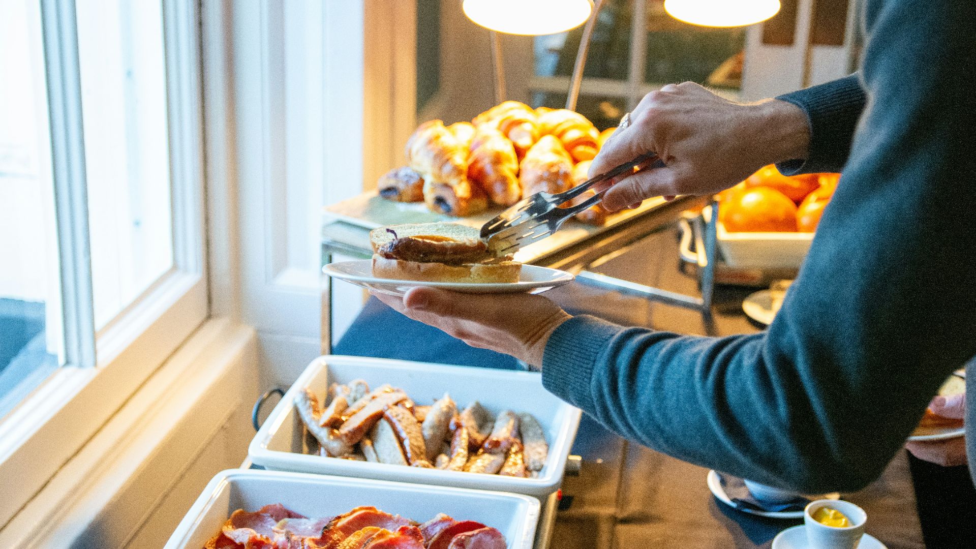 Person serving breakfast buffet with bacon and pastries