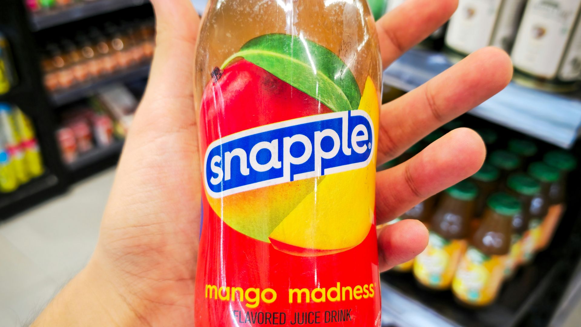 Hand holding a snapple mango madness bottle in store.