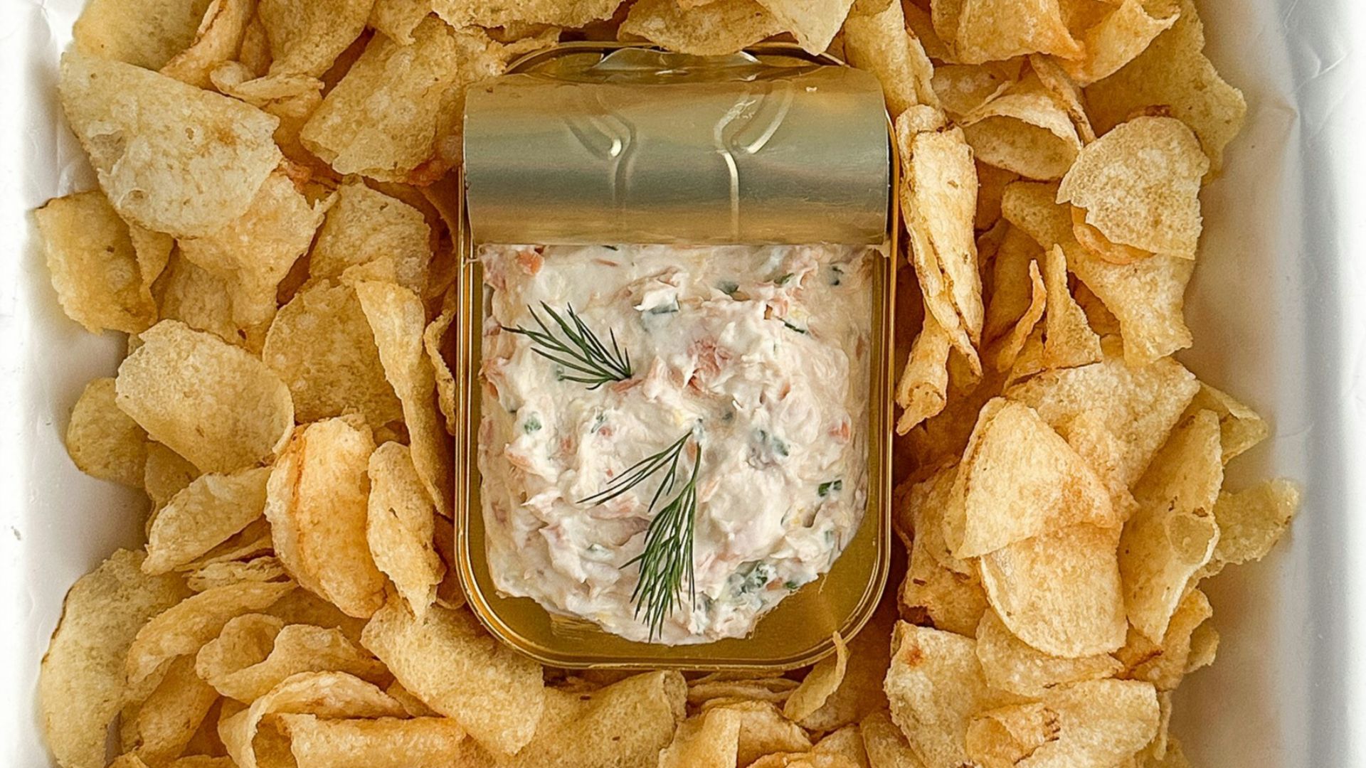 A jar of dip surrounded by potato chips