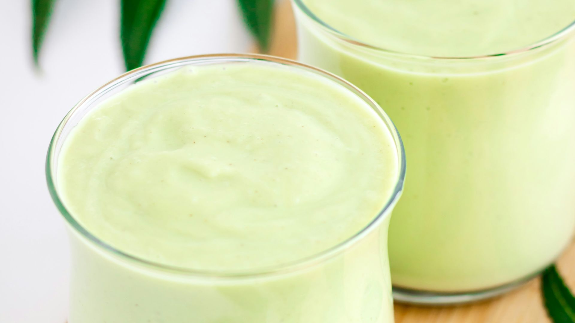 two glasses of green smoothie on a cutting board