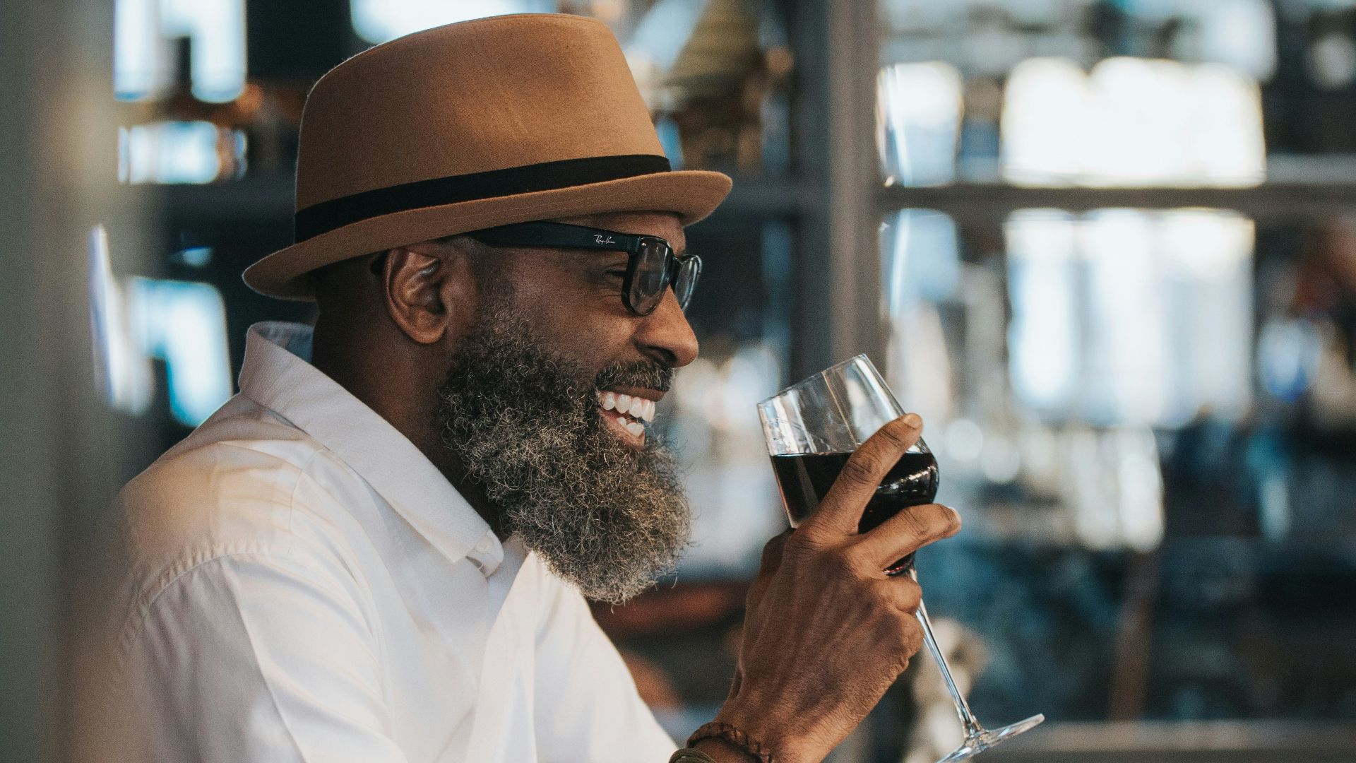 man in white dress shirt and brown hat holding clear drinking glass