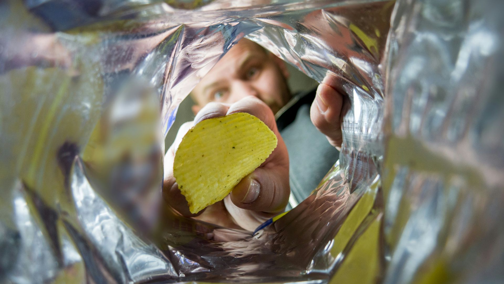 a man holding a cell phone and a potato chip in his hand