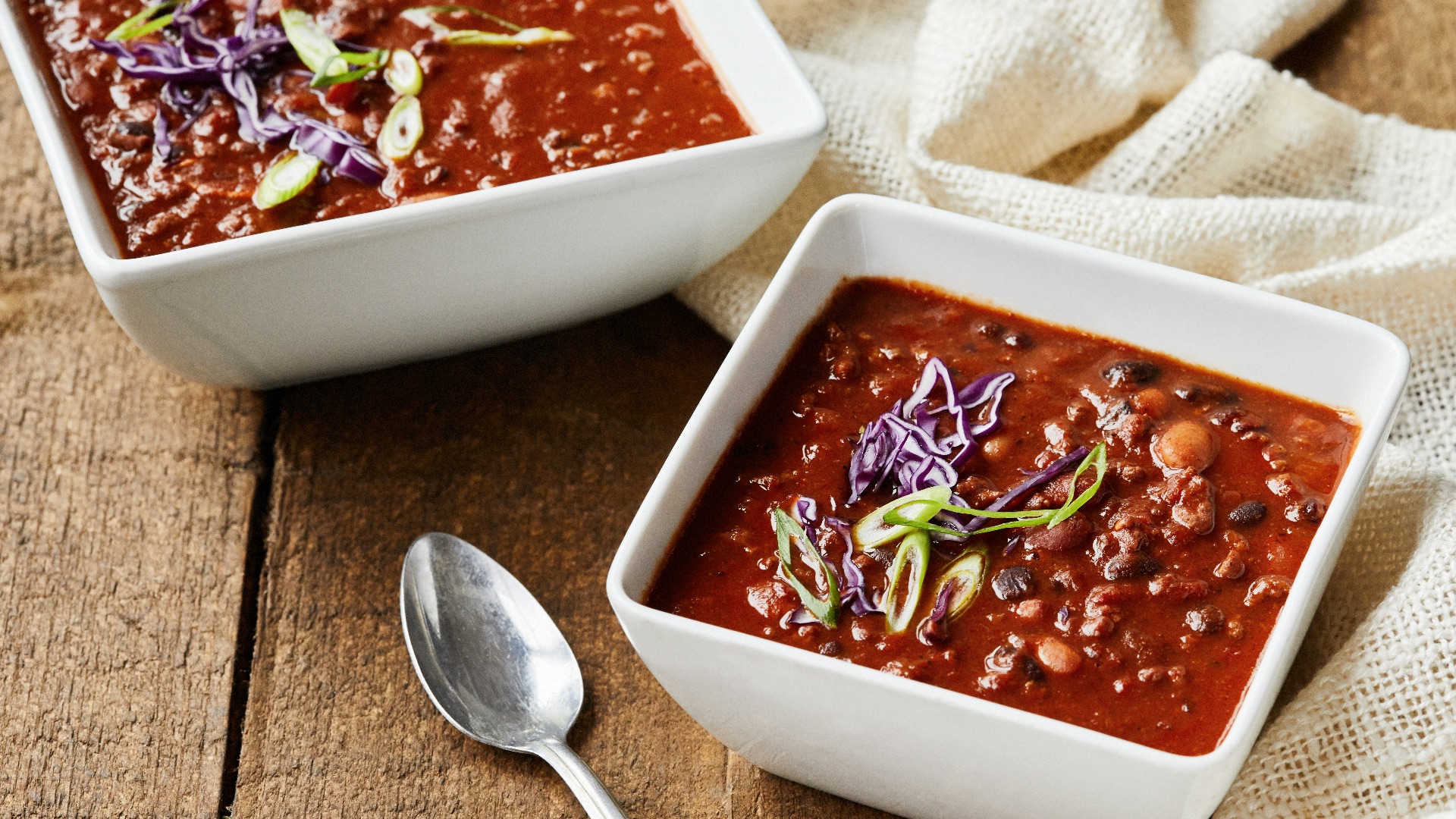 two bowls of chili and a spoon on a wooden table