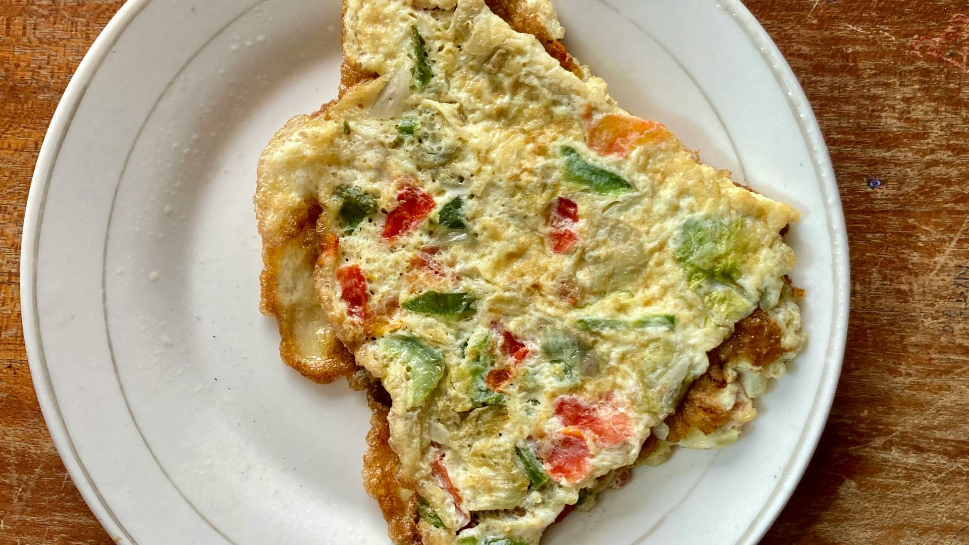 a slice of quiche on a white plate on a wooden table