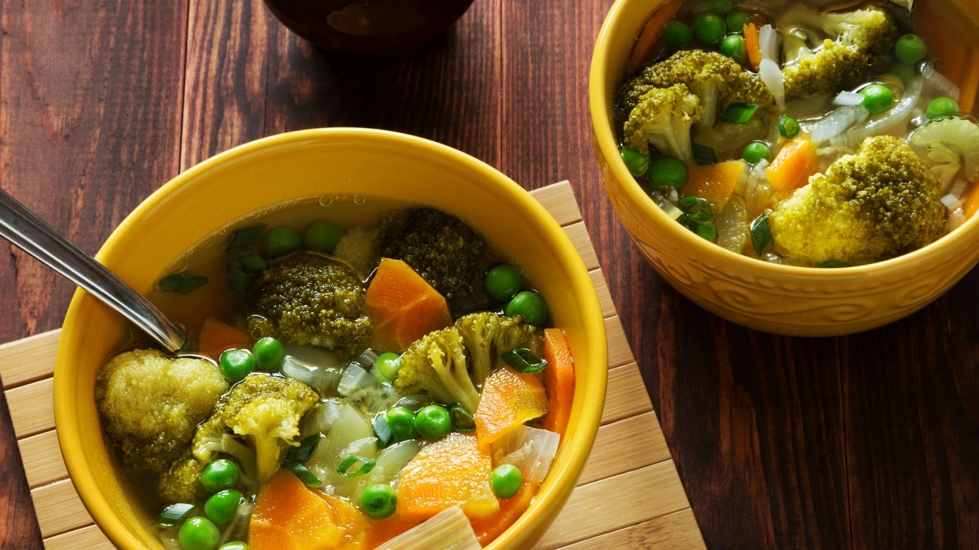 two bowls of soup with peas, carrots and broccoli
