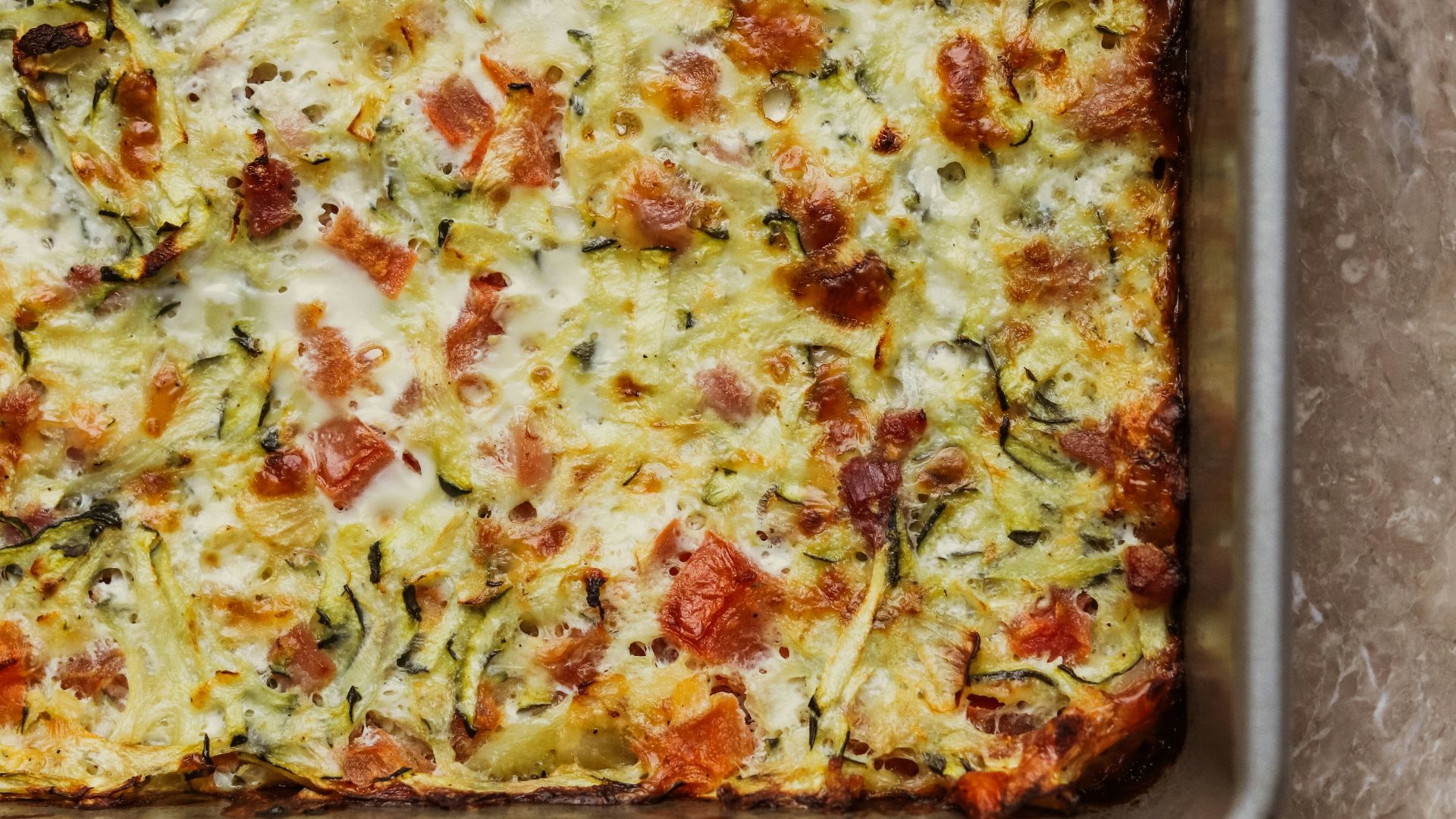 a square casserole dish with cheese and vegetables